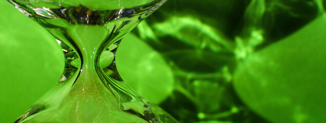 Macro photo, glass hourglass detail, shadows and bright green background.