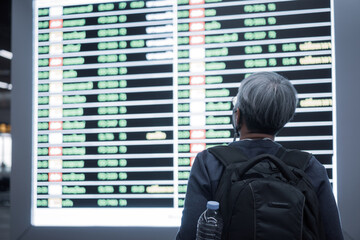 Fototapeta premium Traveler was cancel flights for stop prevent COVID-19 virus disease concept, Senior smart woman traveling backpack standing look flight schedule at airport terminal while world pandemic Corona virus