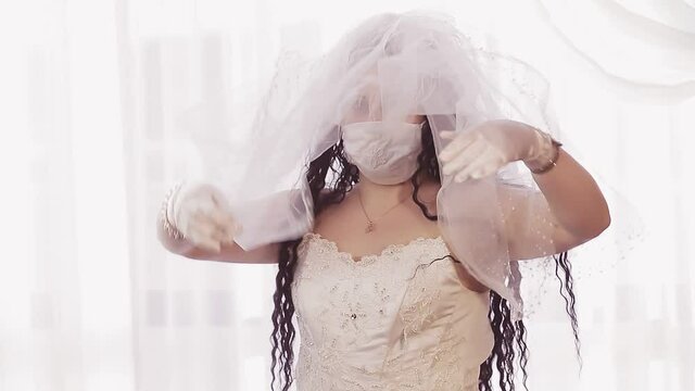 A Jewish bride in a wedding dress and a veil wearing a medical mask covers her head with a veil before the wedding ceremony. Medium plan
