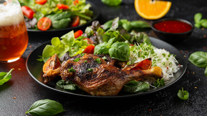 Slow cooked aromatic duck legs with basmati rice and side salad served with orange wedges on black plate