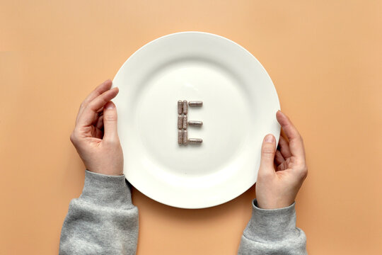 The sign of vitamin " E " from tablets on a white plate. Vitamin E deficiency in the body. Vitamins in food