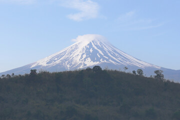 Mount Fuji and the mountain range covered by trees on a clear day.