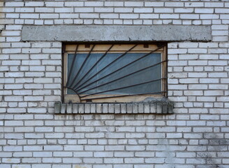 Fototapeta na wymiar A window covered by a metal grate in a white brick wall