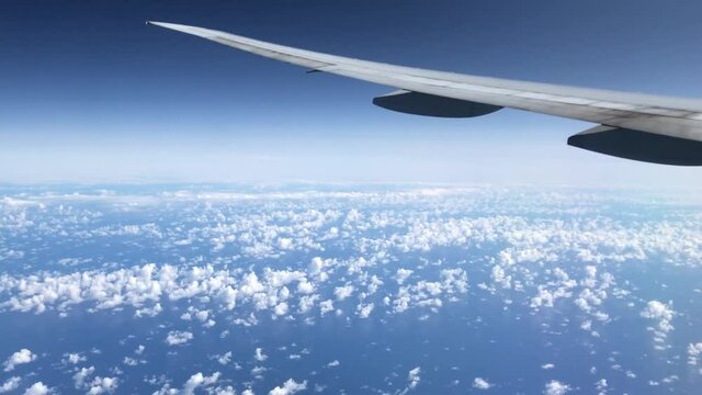 View of a blue bright sky with patchy clouds from the window of a plane with the wing in the scene. 