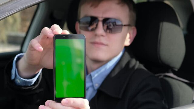 Satisfied man showing smartphone with green screen from car