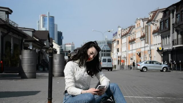 A beautiful hipster girl sits on the street of her city and communicates online