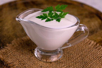 Sour cream in a glass gravy boat with parsley.
Close-up.
