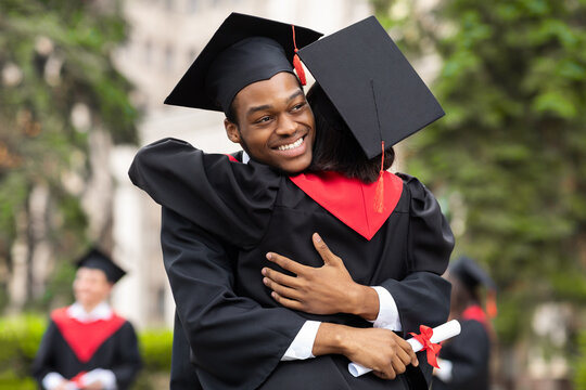 Cheerful black guy hugging his girlfriend while graduation ceremony