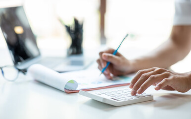 Close up man using calculator and laptop for do math finance on wooden desk, tax, accounting, statistics and analytical research concept