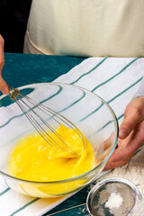 Female hands beat chicken eggs with a hand whisk. The process of making pie dough. The culinary process in the kitchen.