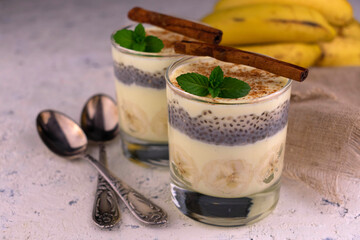 Two glasses with banana yogurt with cinnamon and chia seeds on a white plate.
Close-up.