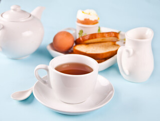 Cup of tea and boiled egg in eggcup on wooden board with crispy toast. Breakfast concept.