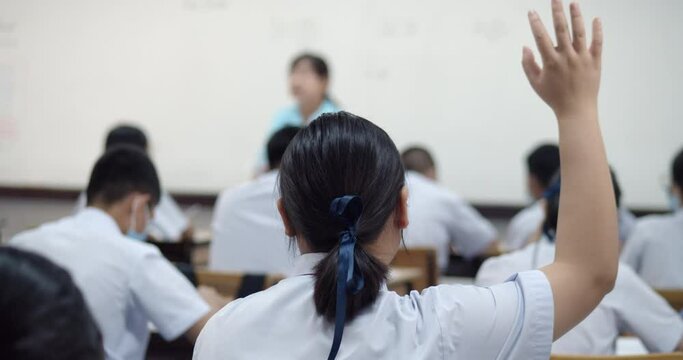Slow motion scene of an Asian high school students in white uniform are studying in classroom and a male student raise his hand to answer a question that a teacher ask them by Q and A teaching method.