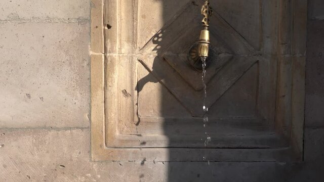 Public metal yellow faucet fountain with drinking clear water flowing in old traditional city