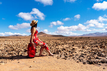 woman on a deserted road with red suitcase to go on a summer vacation
