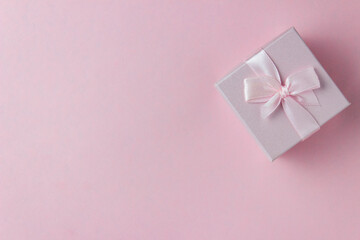 Pink gift box with ribbon tied bow on pink background. Top view