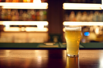 Glass full of fresh foamy beer on wooden counter
