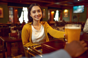 Smiling girl holds glass of beer at counter in bar