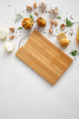 Empty wooden cutting board with homemade bread, spices and greens on white textured vintage background, copy space.