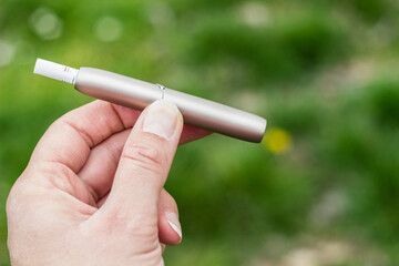 Young woman hand holding and smoking electronic cigarette. Outdoors, nature background, in the park