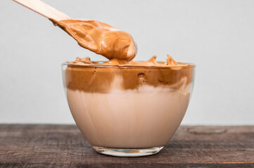 Big cup fluffy coffee with milk and spoon on a wooden table. Coffee drink. Creamy caramel whipped latte. Close