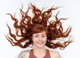 Portrait of smiling girl with red hair infront of white background having long, curly hair around her head