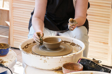 Woman makes clay dishes on small potter's wheel. Master class in the pottery workshop. Creative leisure, hobbies, love to do things with your own hands.