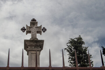 stone cross with treetop and fence clipped on sky background with clouds