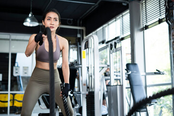 Fototapeta na wymiar Young Asian girl in fitness gym. Asian woman working out in gym doing strength training working out with battle rope. Fitness woman exercising indoor in fitness center. Female with in gym.