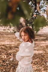 Nice girl with curly hair under an oak tree. Spring, autumn. Blue sky with clouds. 