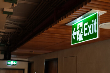 Green fire escape sign hang on hotel ceiling. Green exit sign. LED green Emergency exit sign in the ceiling of modern hotel building.