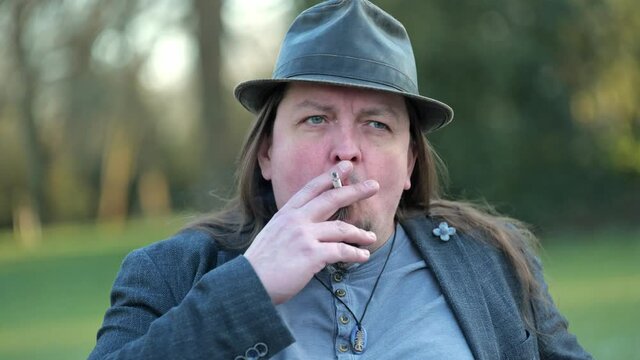[4k] close up of long haired goatee man smoking wearing a hat