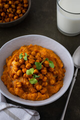 Thick pumpkin soup with baked chickpeas and radish sprouts in a plate with a glass of milk on the table, delicious healthy dinner