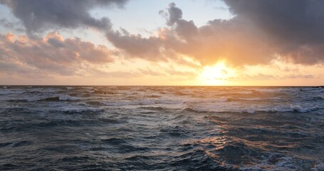 Baltic sea shore under a blue sky with glowing pink and golden sunset clouds after the storm. Crashing waves. Nature, environmental conservation, ecotourism. Picturesque panoramic scenery