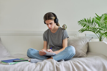 Obraz premium Male teenager with pet green parrot on his shoulder, with textbooks