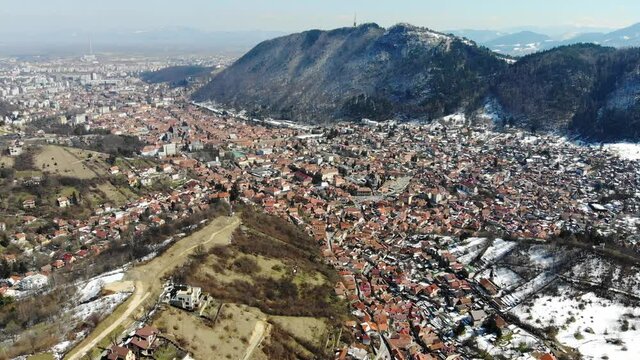 Panoramic aerial shot of historic city center of Brasov and Carpathian mountains in the background rotaing to reveal the entire city