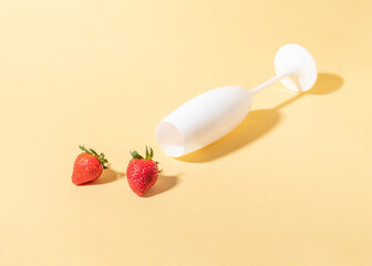 Sunny spring table composition with white champagne glass and strawberries against bright peach puff background.