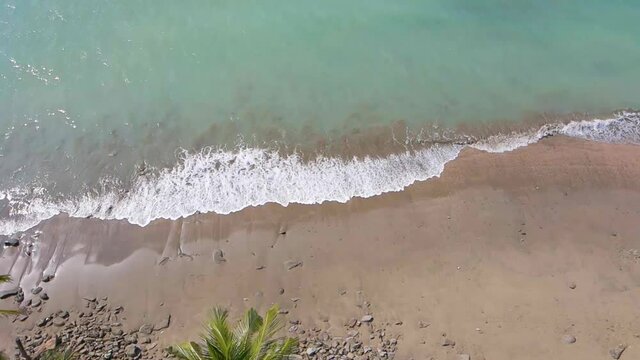 Sea waves breaking on the beach slowly while drone flying backward over palm trees and rocky shore. Aerial view. Saint martin island, Bangladesh