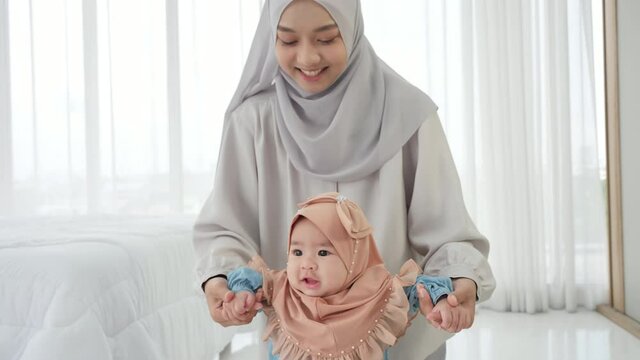 Happy asian family Baby girl 6 months old in traditional hijab clothing taking her first steps andthe help of her mother in bedroom. slow motion
