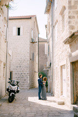 Fototapeta na wymiar Bride in stylish blue dress and the groom hugging against the background of beautiful white houses in the old town of Perast, 