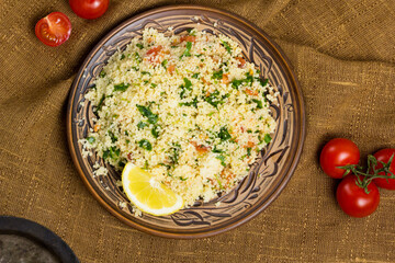 Traditional Arabic salad or Tabbouleh on ceramic plate, healthy vegetarian dish with couscous, tomatoes, parsley, mint
