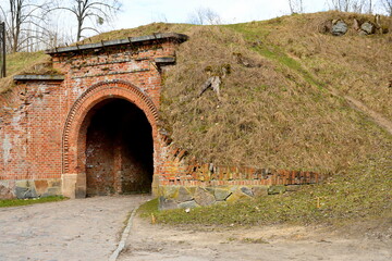 Close up on an old abandoned wooden gate between two hills with an arch and some decorative elements seen during a hike on a spring sunny day on a Polish countryside next to a dirt path and pavement