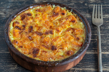 Baked yellow pumpkin in milk sauce with honey and egg on a plate on the wooden table, top view. Vegetarian food