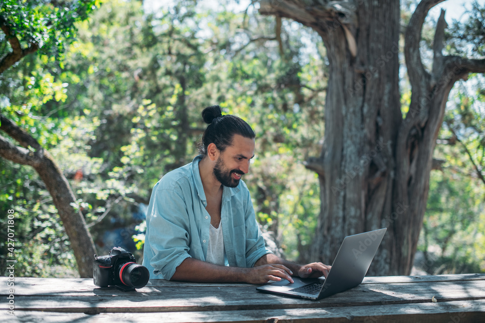 Wall mural Male photographer working on a laptop outdoors in a camping