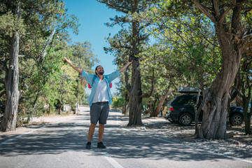 Fototapeta premium Male tourist stands on the road cheerfully raising his hands
