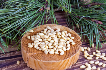 Fresh peeled pine nuts with green coniferous branches on light wooden background.