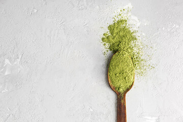 Wooden spoon with green natural powder on gray concrete background with copy space.