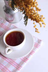 a branch of mimosa and a cup of tea on tablecloth flat lay