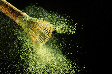 Bamboo whisk with flying matcha tea powder on a black background.