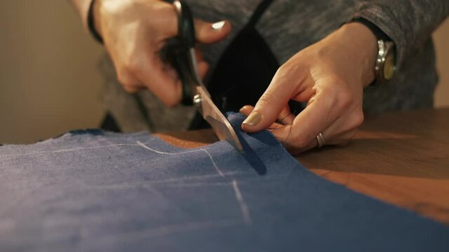 Hands cut the fabric with tailor's scissors, cutting a piece of fabric the concept of a fashion designer. Blue fabric for sewing clothes.
